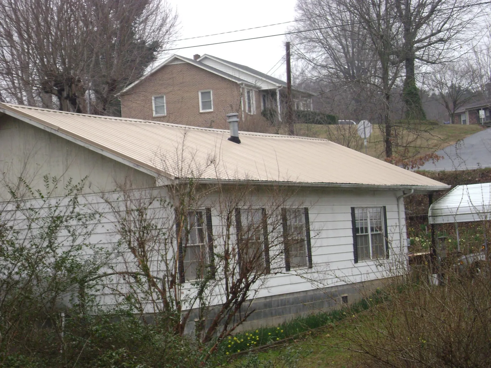 Tan metal roof on a white sided house set into a hillside — Commercial Roofing by Roofing Brothers in Ridgeway