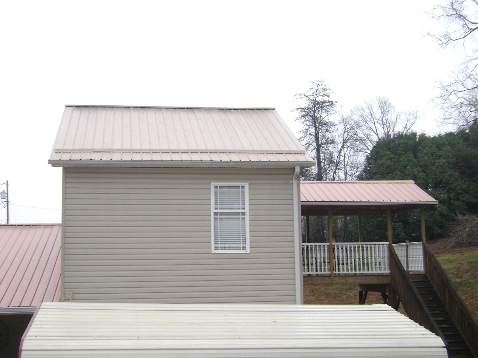 Tan metal roofs on a two story addition and attached porch, from a Roof Replacement job in Ridgeway